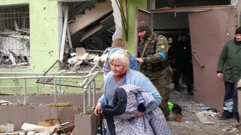 Sergei Orlov A wounded woman leaves the maternity and children's hospital in Mariupol after it was bombed by Russian forces