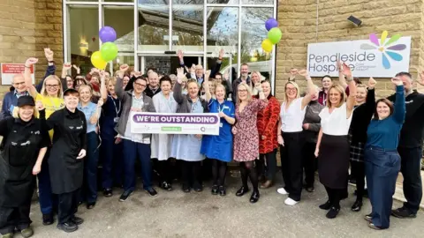 Pendleside Hospice handout Pendleside Hospice holding a banner saying outstanding to celebrate its CQC rating
