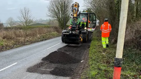 Ollie Conopo/BBC Digger-like machine moves across road surface under repair