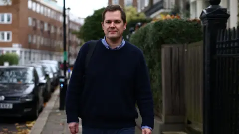 Getty Images Jenrick walks down a street carrying a backpack.