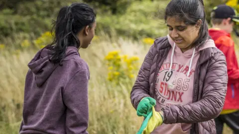 Action for Conservation Two girls in a wild grassy area donning gloves