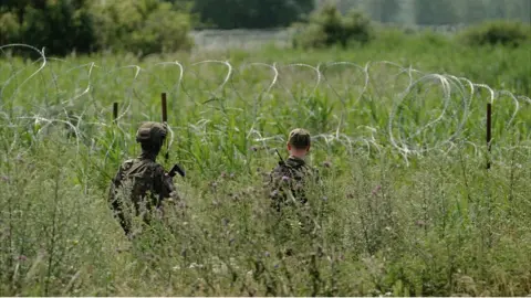 Matthew Goddard/BBC Polish border guards patrol alongside a barbed wire fence