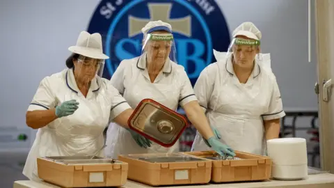 PA Media Dinner staff wearing PPE dispense a hot lunch to pupils at St John the Baptist Primary School, in west Belfast