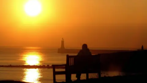 PA Media Person watches the sun rise over Tynemouth bay