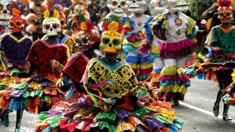 AFP People in colourful dress and skull masks in the parade