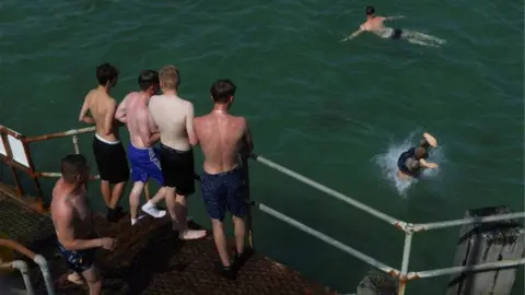 Reuters A man dives from the railing of the stairs leading to a pier as people look on while enjoying the hot weather at Bournemouth Beach