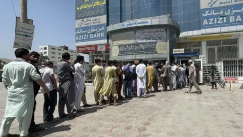 Anadolu Agency via Getty Images Afghan people line up outside AZIZI Bank to take out cash as the Bank suffers amid money crises in Kabul, Afghanistan, on August 15, 2021.