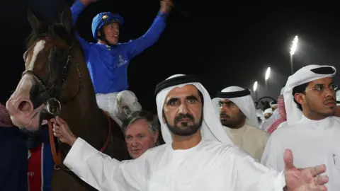 AFP Sheikh Mohammed Al Maktoum holds the bridle of Electrocutionist after it wins the Dubai World Cup, as jockey Frankie Dettori celebrates (25 March 2006)