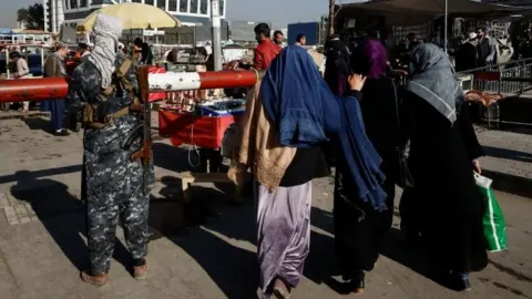 Reuters Women walk past a Taliban guard