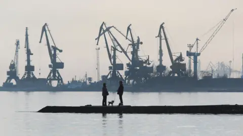 Getty Images A couple walks a dog on a pier at a coast of the Sea of Azov in Ukraine's industrial port city of Mariupol on February 23, 2022