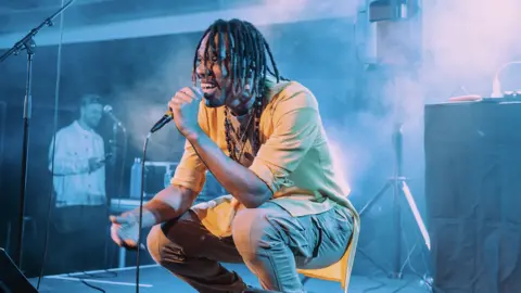 Plaster A man crouching down and singing on a microphone