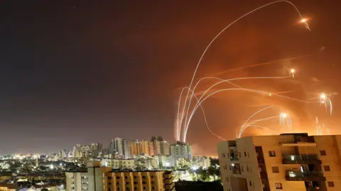 Reuters Streaks of light are seen as Israel's Iron Dome anti-missile system intercepts rockets launched from the Gaza Strip towards Israel, as seen from Ashkelon, Israel (12 May 2021)