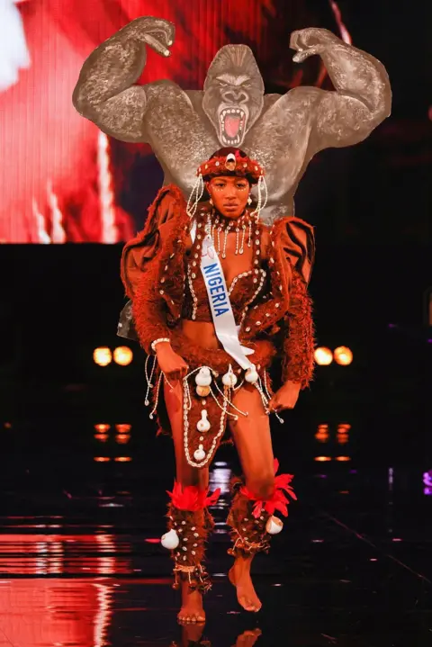 Reuters A woman walks down a catwalk with a cut-out image of a gorilla, and an outfit including cowrie shells and red feathers.