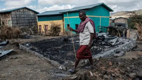 Getty Images Addis Sissay, 49, walks in front of his destroyed house in the village of Bisober, in Ethiopia's Tigray region on December 9, 2020