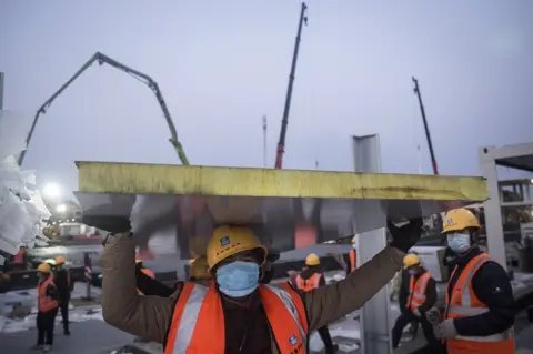 Getty Images A construction worker is pictured amidst heavy machinery on the site of Huoshenshan hospital, under construction