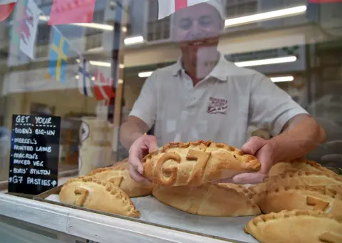 PA Media A baker puts a pasty in his shop window with G7 marked in pastry