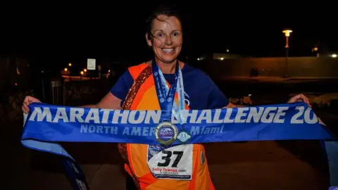 World Marathon Challenge Sally Orange with a banner after completing the challenge