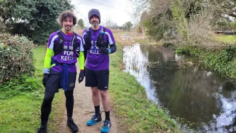 Family handout John Fielding (left) and Michael Pendry (right) standing by a lake wearing purple running gear