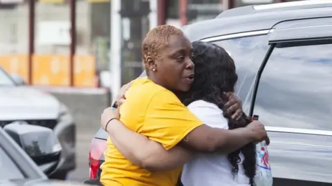 EPA Two people hug near the scene of a shooting at the Tops Friendly Market supermarket in Buffalo, New York on 14 May