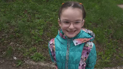 little girl with glasses smiles at the camera