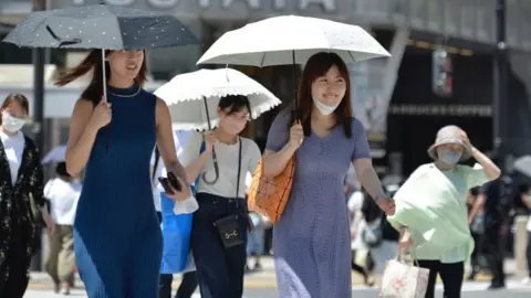 Getty Images People walk on the street using an umbrella to protect themselves from the sun on June 27, 2022, in Tokyo's popular Shibuya district in Tokyo, Japan.