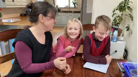 BBC Susanne Wilding at a desk with her two children, a girl and boy, as they do a lesson