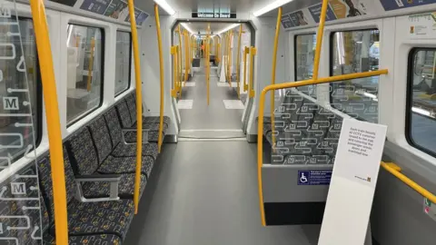 Interior of train showing grey and yellow seats down the sides of the carriages