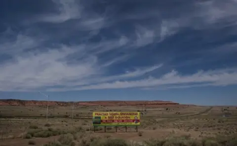 AFP Sign in desert saying "practice social distancing and self-isolation"