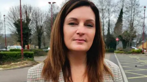 Woman with long brown hair standing in a car park