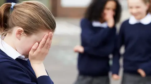 Getty Images Schoolchildren whispering in playground about another child