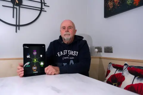 BBC Stephen West in his home holding an iPad showing energy coming in and going out