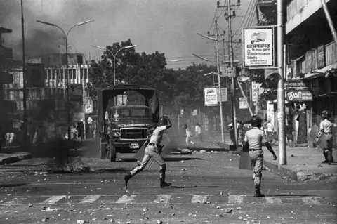 Shahidul Alam People throwing stones in the street towards police carrying shields