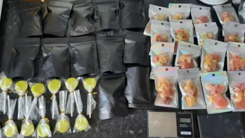 Wiltshire Police Yellow cannabis lollies and bags of red and orange cannabis sweets laid out on a counter