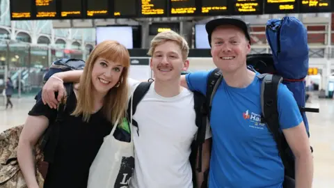 PA Media Becky Moriarty, Jared Hill and Rory Leighton in Paddington Station in London, they are travelling by train to the Glastonbury Festival