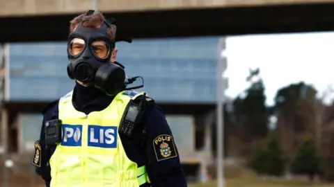 Police officer wearing gas mask outside Sweden security service HQ on Friday