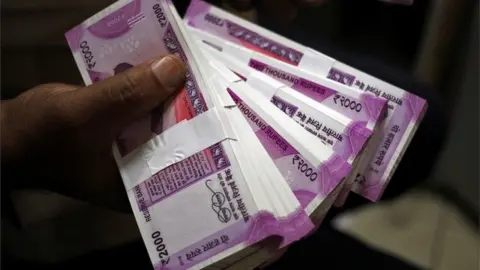 Reuters A bank worker holds wads of Indian rupee banknotes