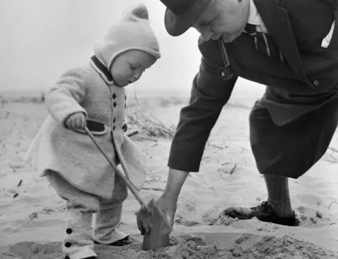 Historic England/John Laing Collection man helps child build sandcastle