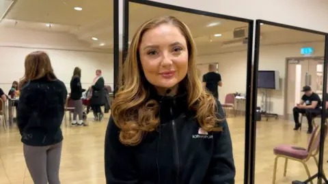 Carroll Weston/BBC Woman with long blonde hair wearing a black top in front of a dancing mirror