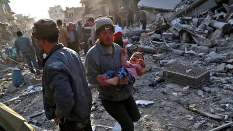 AFP A Syrian man carries a child following a reported air strike on the rebel-held town of Atareb in northern Syria on 13 November 2017