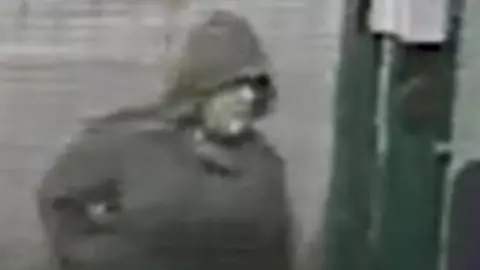 A blurry black and white image of a white man wearing a dark hooded jacket