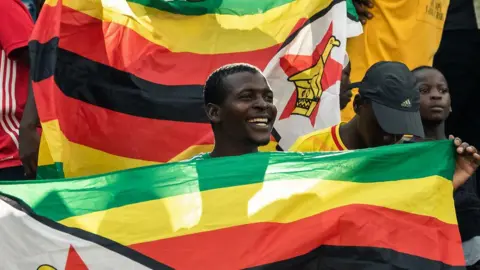 AFP A Zimbabwe Warriors's supporter holds a flag aduring their 2019 African Cup of Nations group G qualifying football match between Zimbabwe and Congo Brazzaville at the National Sports stadium in Harare, on March 24, 2019.