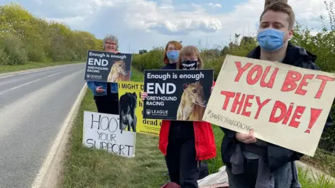 Shut Down Henlow Greyhound Stadium People holding signs by the side of the road.