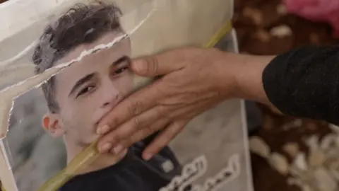 Hand of the four brothers' mother on graveside photo of one of her sons