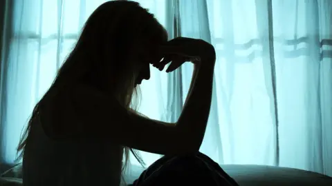 Silhouette of woman sitting in bed by window