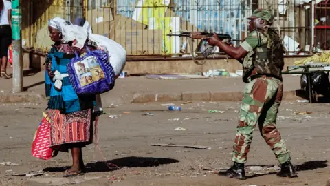A vendor scurries for cover with her wares as soldiers disperse demonstrators on August 1 2018, in Harare, Zimbabwe