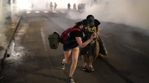 Getty Images Two protesters flee through tear gas after federal officers dispersed a crowd of about a thousand at a courthouse in Portland, 21 July 2020