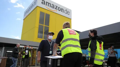 Getty Images Striking Amazon employees stand outside an Amazon warehouse during the coronavirus pandemic on June 29, 2020 in Kobern-Gondorf near Koblenz, Germany