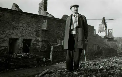 Roger Tiley Mr Coles' home is demolished as he looks on in 1983 - he had lived in the miners cottage at The Ranks in Abercarn, Caerphilly, all of his life