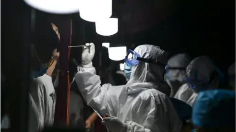 Getty Images A medical worker collects swab from a resident for nucleic acid testing at dawn