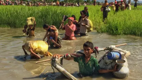 BBC Rohingya children and adults wade through water carrying their possessions